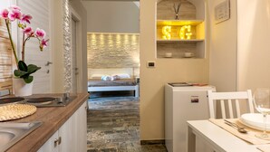 A modern hotel room with a kitchen area, a dining table set with a glass of wine, and a bed with a view.
