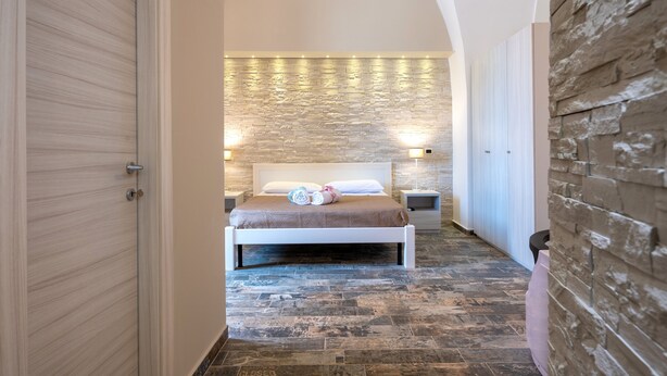 A bedroom with a bed, nightstands, a stone wall, and an arched ceiling.