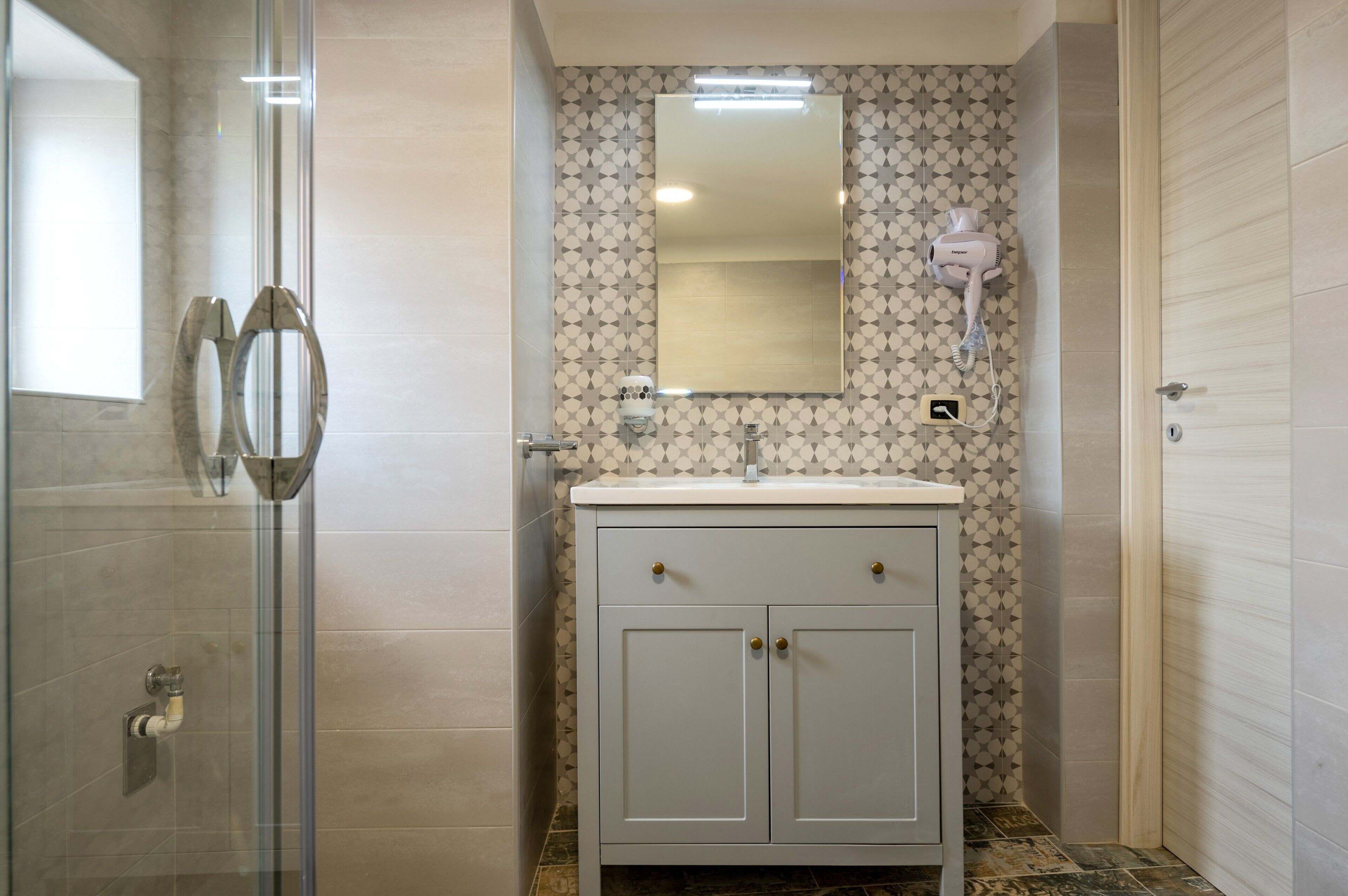 A bathroom with a glass shower enclosure, a vanity with a mirror, and patterned wall tiles.