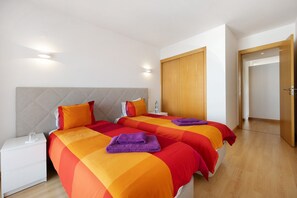 A hotel room with two beds, a nightstand, a wooden wardrobe, and a door leading to another room.
