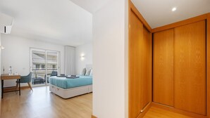 Un dormitorio moderno con cama, escritorio y silla. Se ve un balcón desde la ventana.