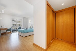 A modern bedroom with a bed, a desk, and a chair. There is a window with a view of a balcony.