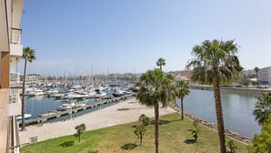 Un puerto deportivo con numerosas embarcaciones amarradas, rodeado de palmeras y un césped.