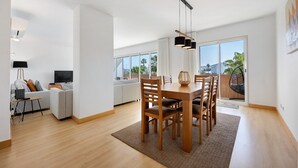 Una sala moderna con comedor, ventanas amplias y vista a palmeras.
