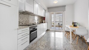 Una cocina moderna con armarios blancos, encimera de granito y comedor con mesa y sillas.
