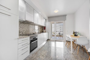 A modern kitchen with white cabinets, a granite countertop, and a dining area with a table and chairs.