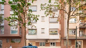 Ein mehrstöckiges Gebäude mit Ziegelgliederung, Fensterläden und ein Baum mit grünen Blättern im Vordergrund.