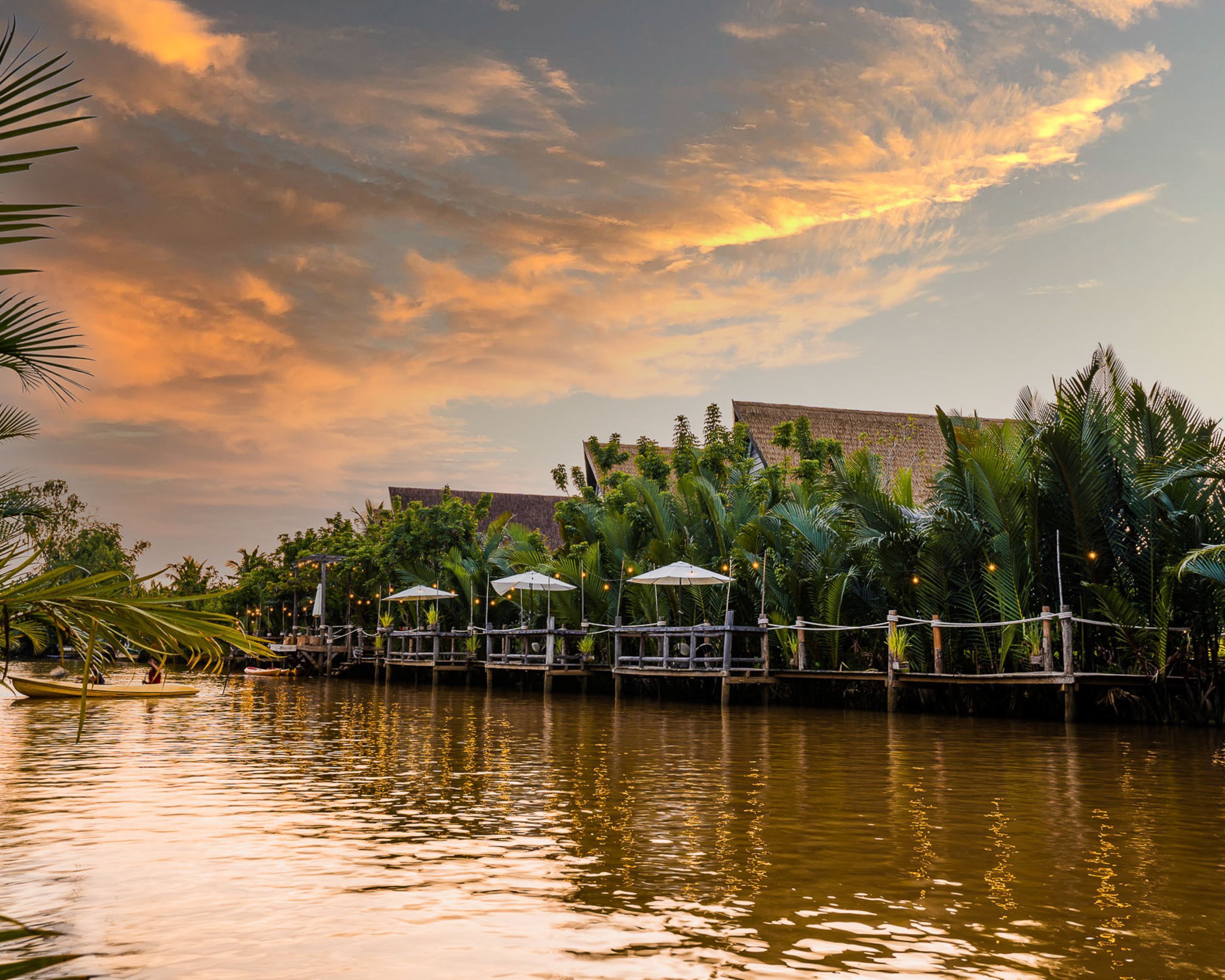 A waterfront area with a wooden dock, umbrellas, and tropical vegetation.