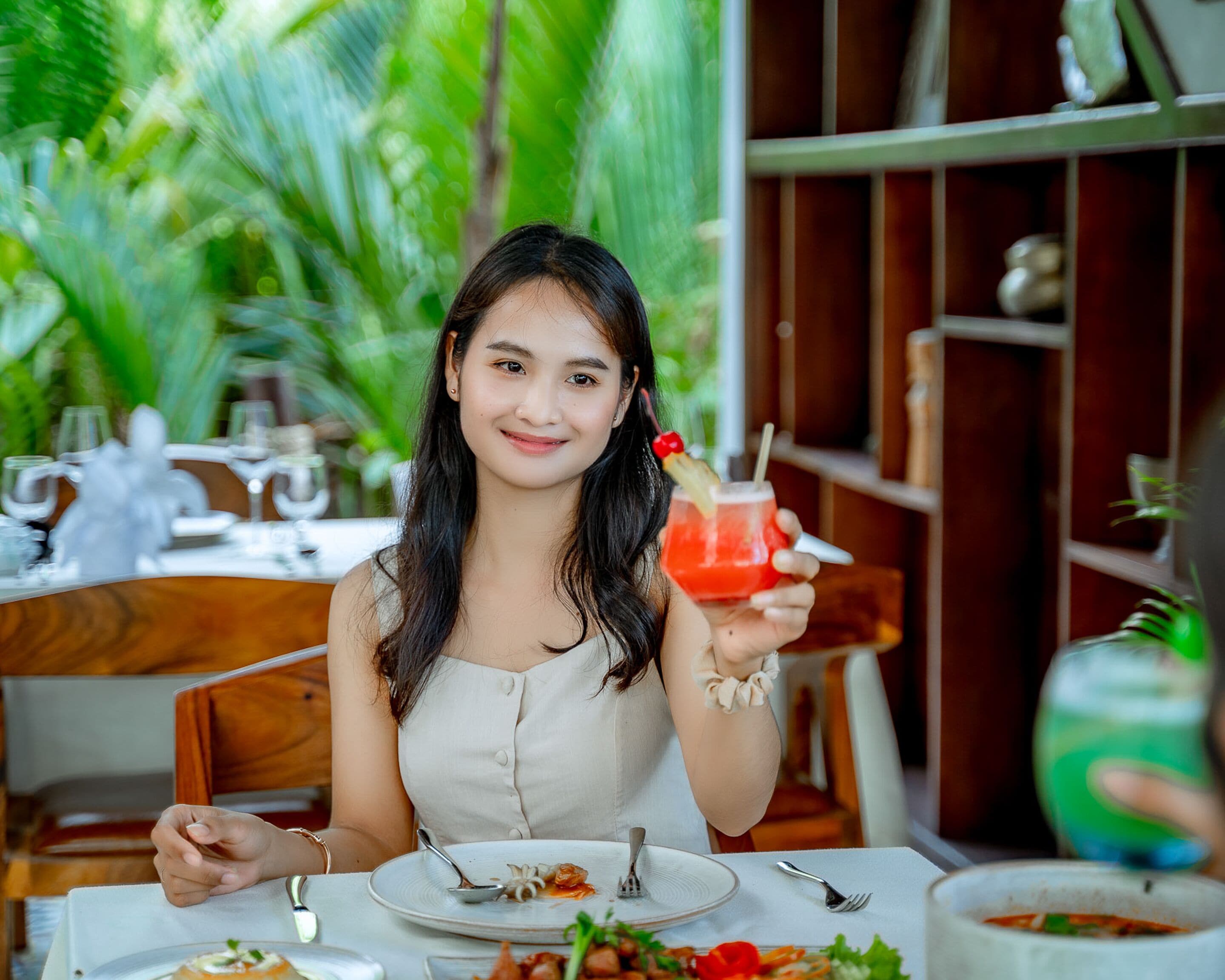 Iemand zit aan een tafel, met een drankje in de hand, een bord met restjes eten en een glas water.