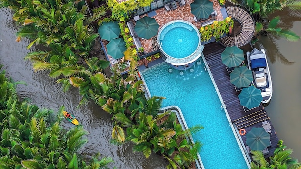 Vista aérea de un resort con una piscina central rodeada de exuberante vegetación y palmeras.