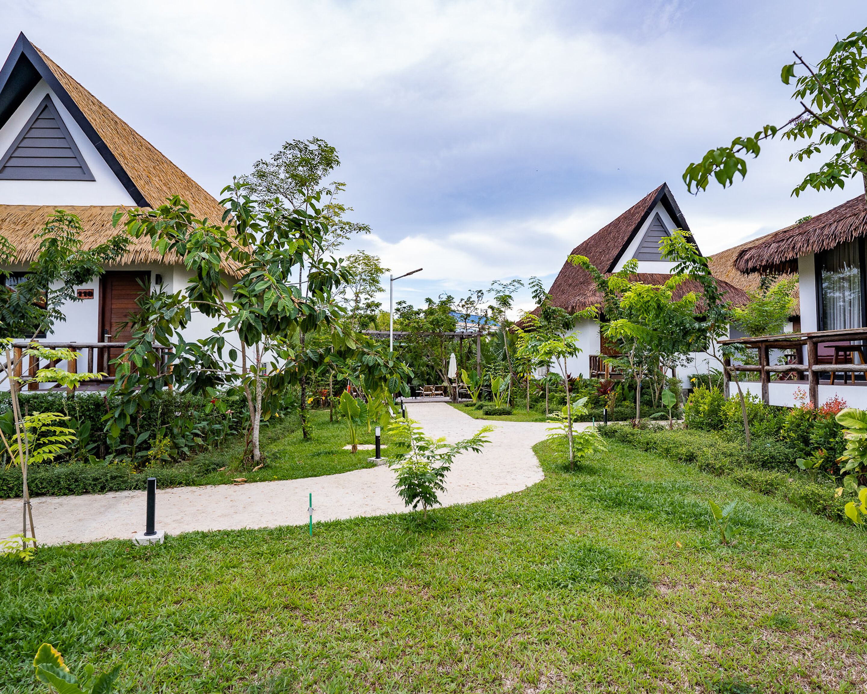 Un resort con cabañas de techo de paja, un camino central y exuberante vegetación.
