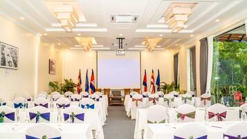 A conference room with rows of tables, chairs with bow ties, a projector screen, and flags.