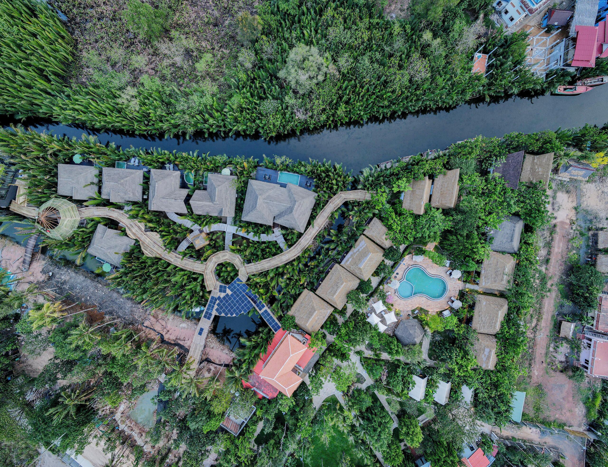 Oversigtsbillede af et resort med flere huse i bungalowstil, et centralt cirkulært område med en springvand og en swimmingpool.