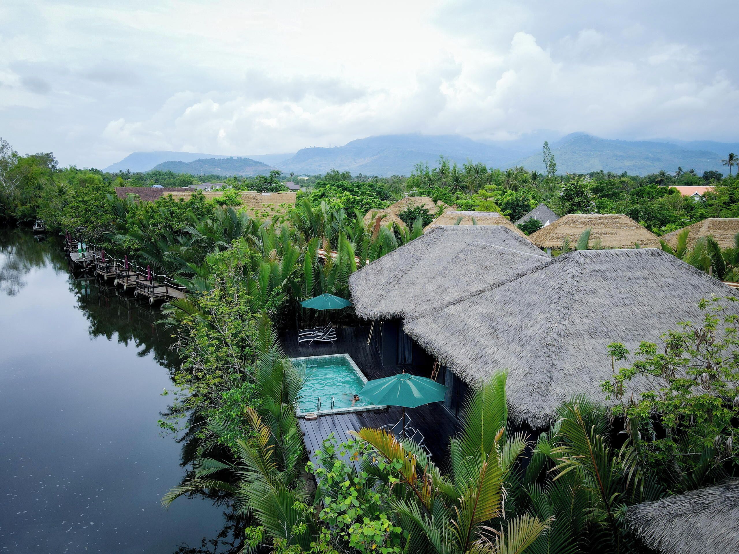 A resort with thatched-roof huts, a swimming pool, and lush greenery.