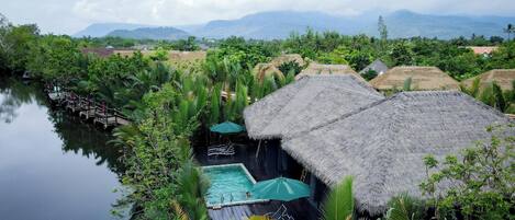 A resort with thatched-roof huts, a swimming pool, and lush greenery.