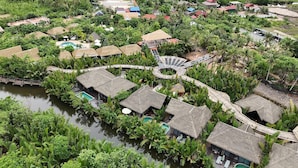Vista aérea de un complejo turístico con bungalows de techo de paja, un paseo central circular y una piscina.