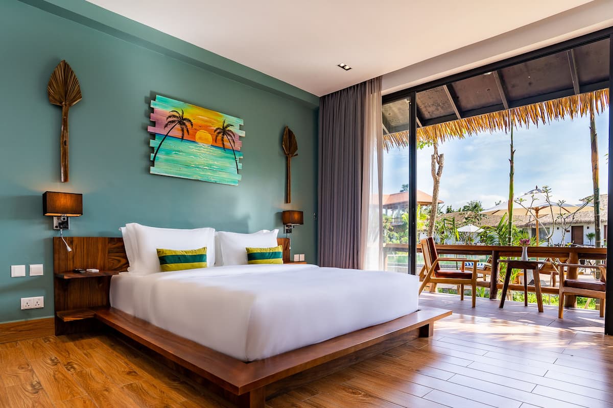 A spacious bedroom with a large bed, wooden headboard, and a view of the outdoor area through a glass door.