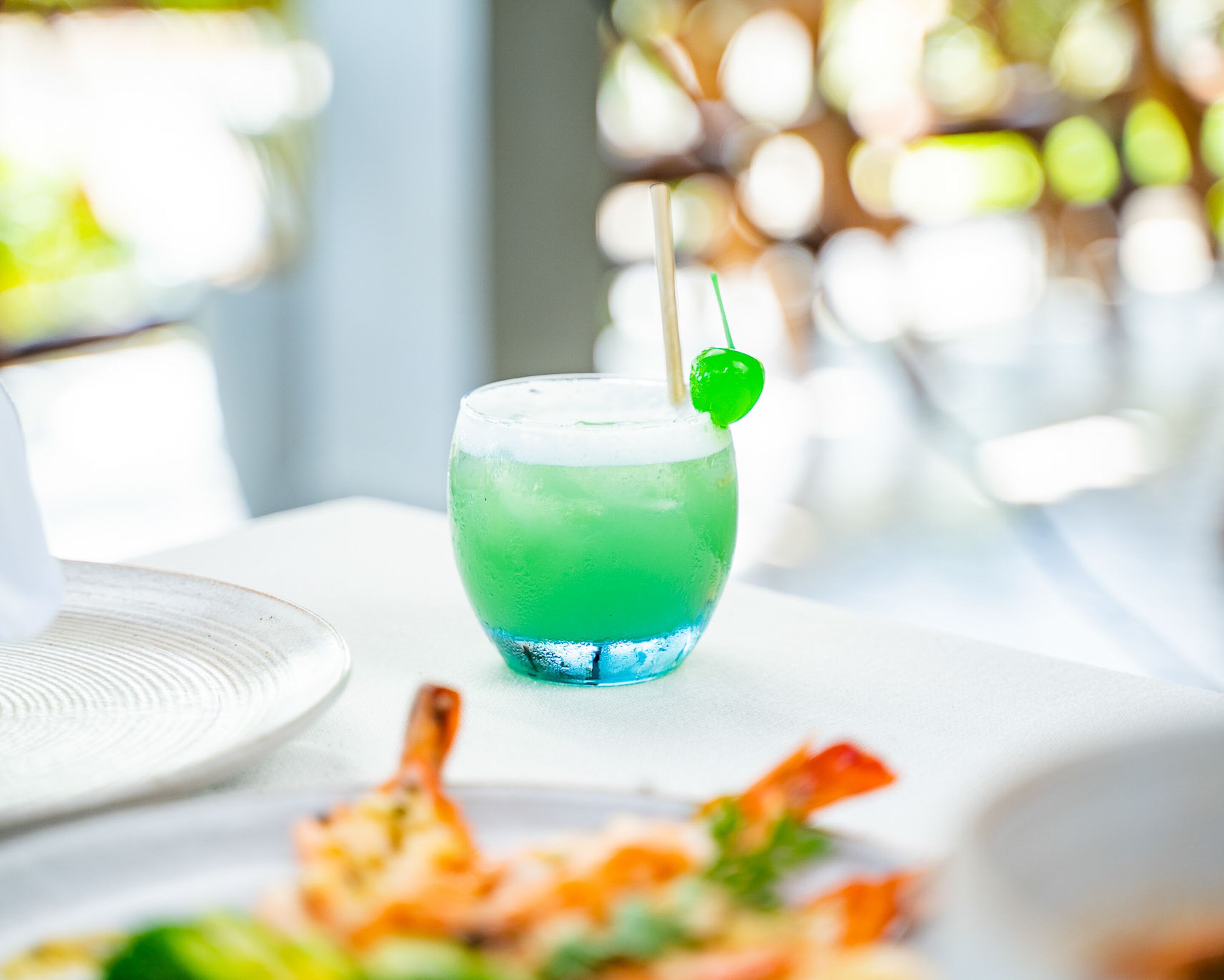 A glass of green drink with a lime garnish on a white table.
