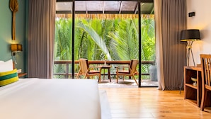 Habitación de hotel con una cama grande, un balcón con muebles de madera y vistas a exuberante follaje.