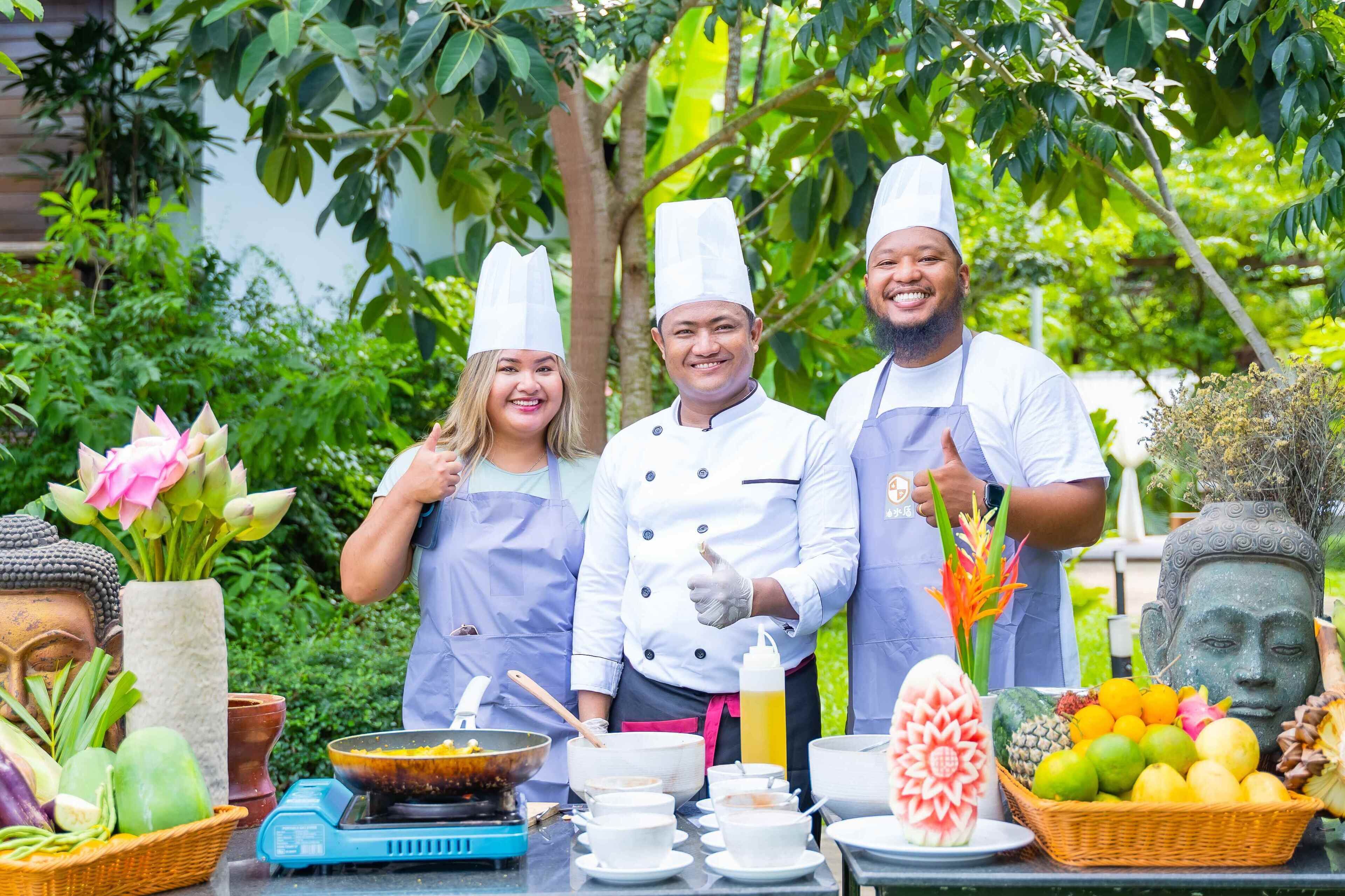Three chefs in white uniforms and aprons standing in front of a table with cooking utensils and ingredients.