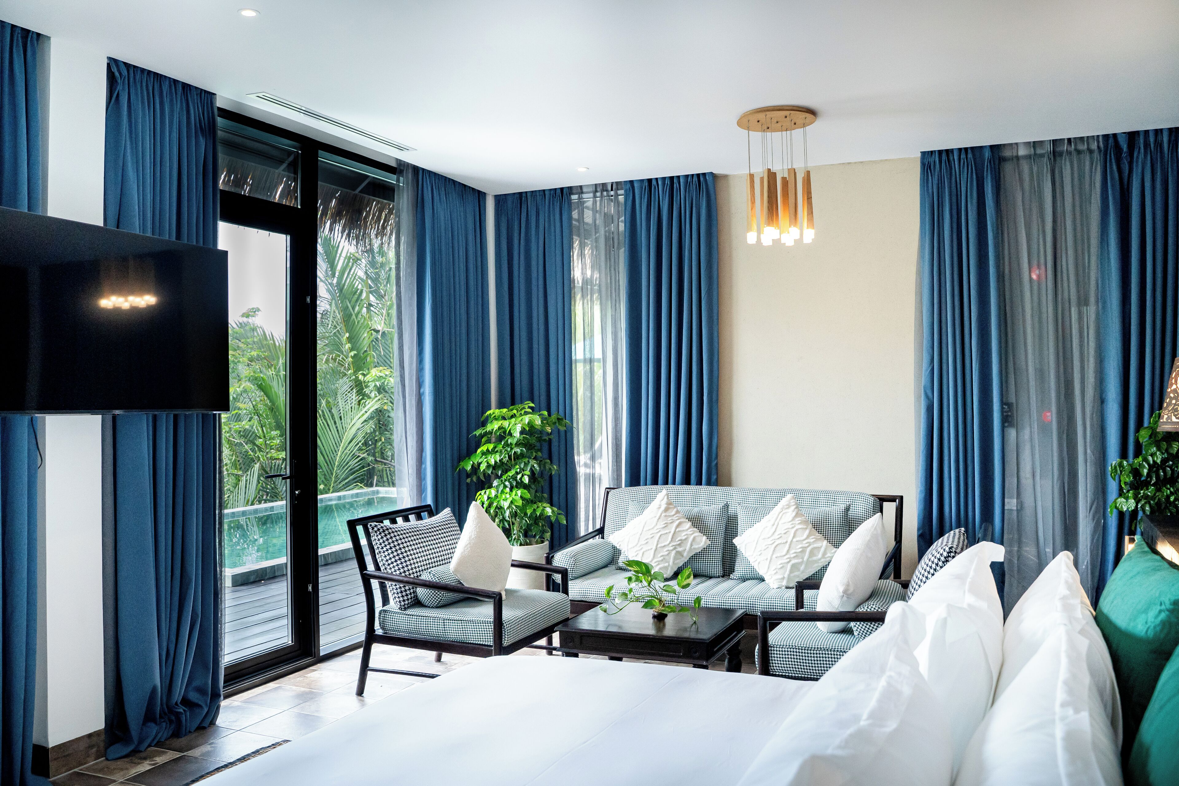 A modern hotel room with a sofa, armchairs, a TV, and a balcony with curtains.