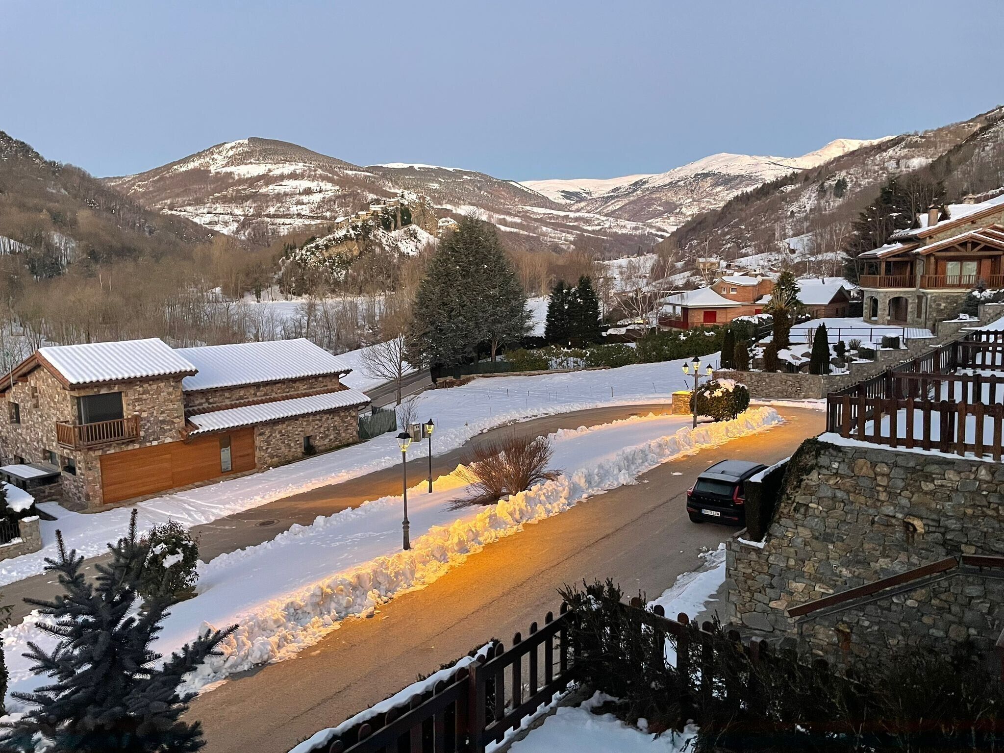 A snow-covered mountain village with stone buildings, a road, and a car.