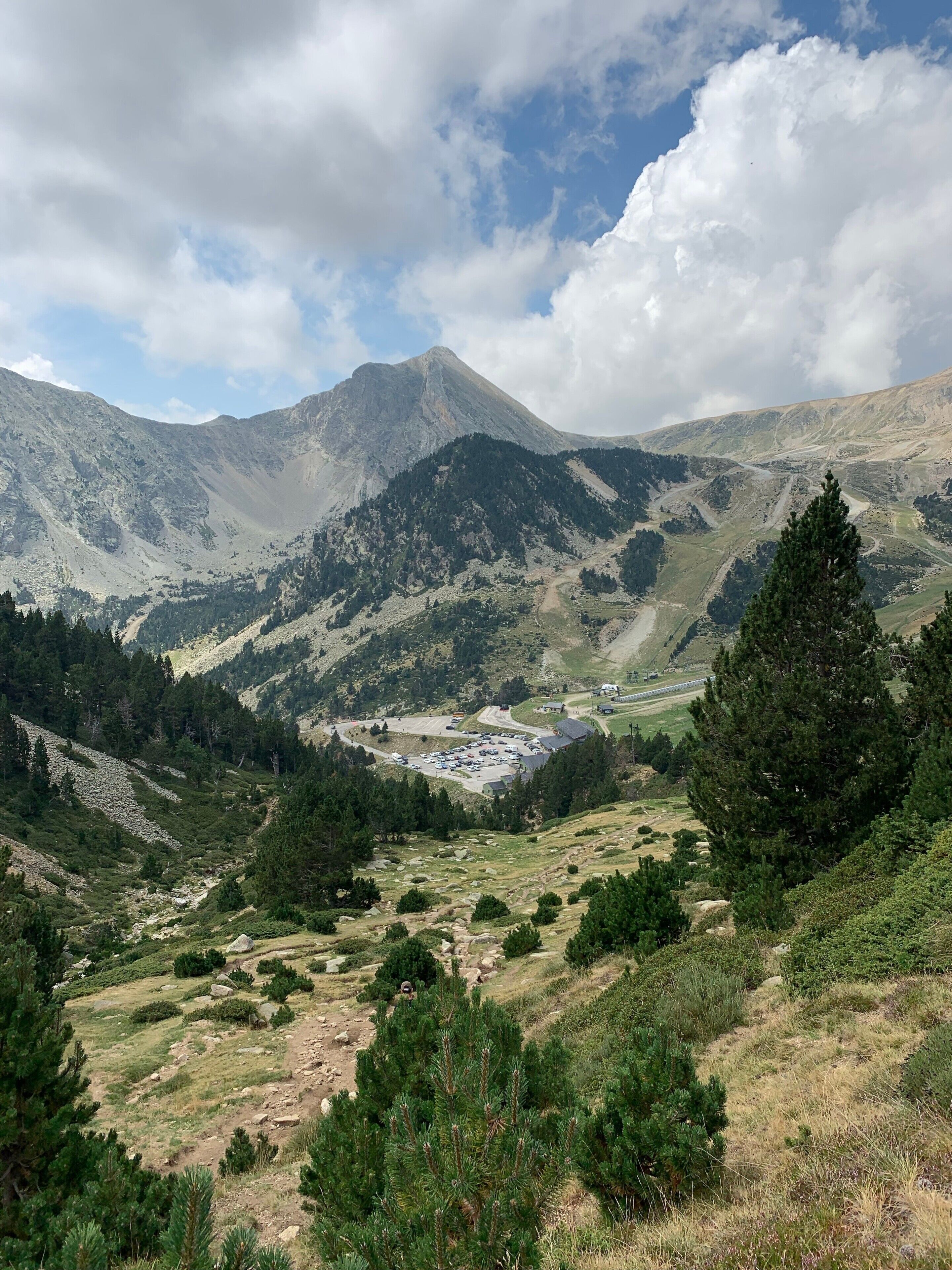 Paesaggio montuoso con un'area di parcheggio, edifici e una strada.