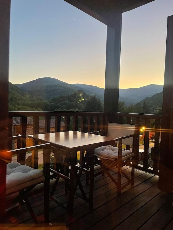 Una terraza de madera con una mesa y sillas, con vistas a un paisaje montañoso.