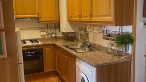 Een keuken met houten kastjes, een wasmachine, een fornuis en een spoelbak.