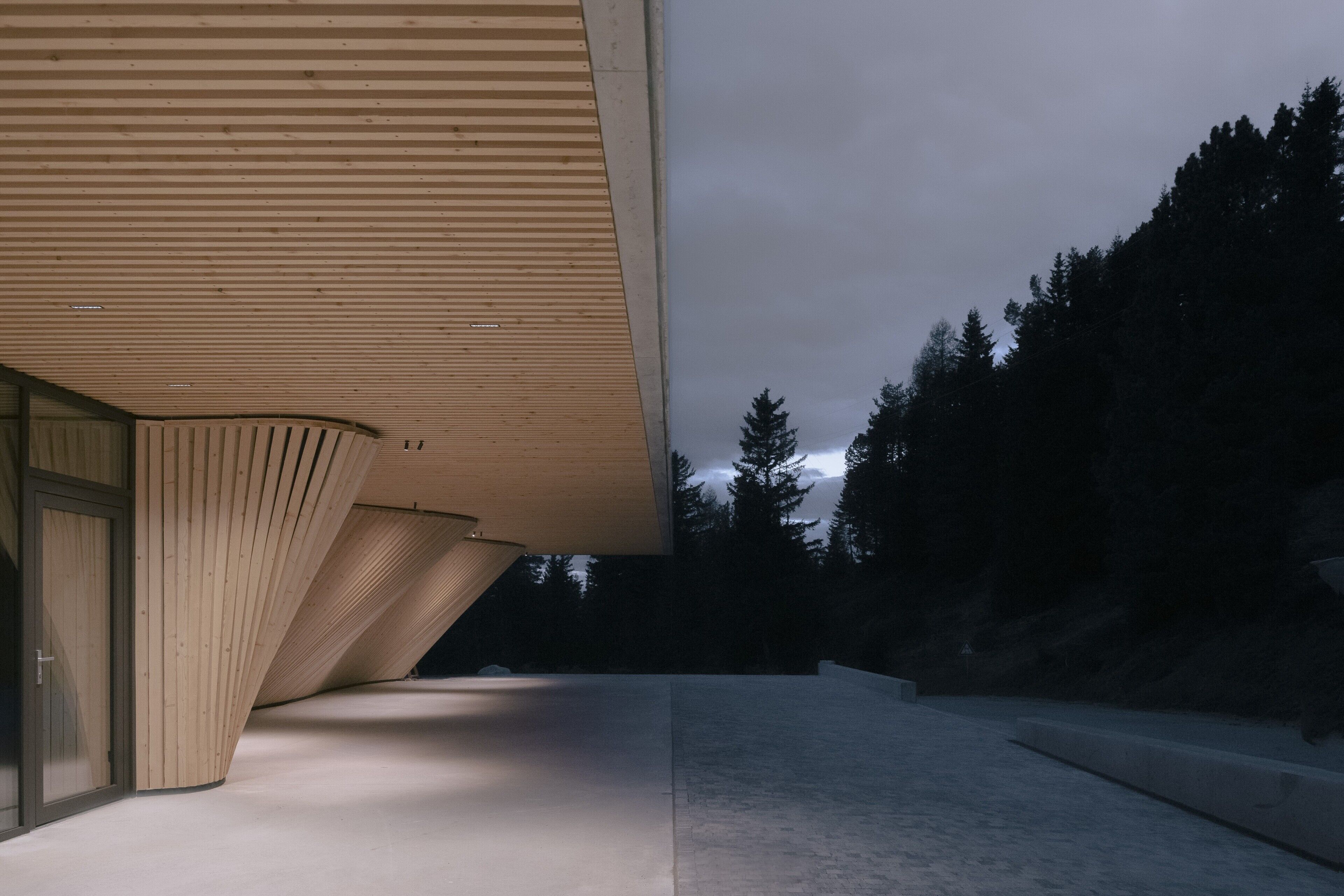 Ein modernes Gebäude mit einem geneigten Dach und einem Betonweg, der zu einer Holztür führt.