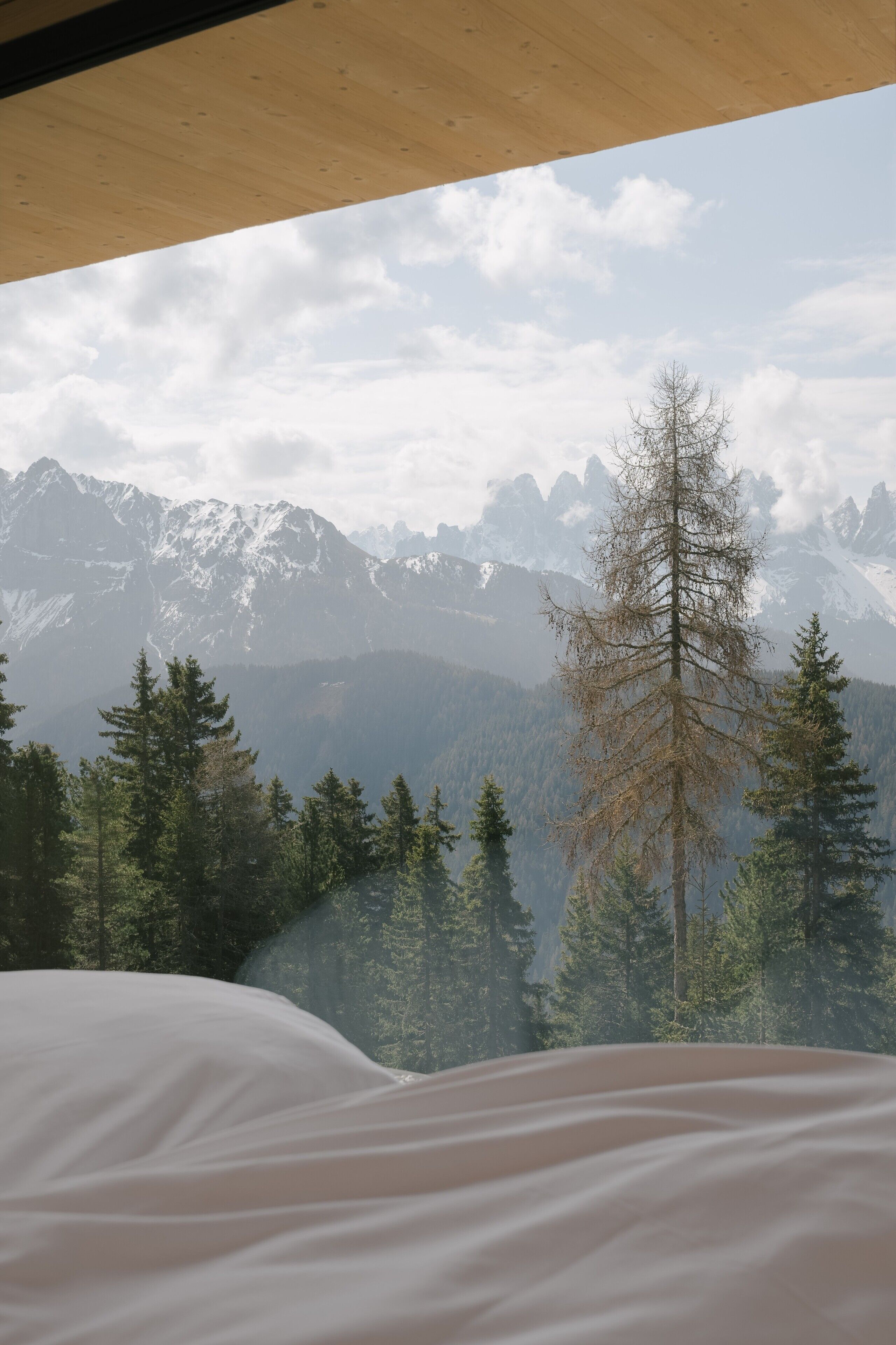 Ein Bett mit Blick auf Berge, einer Holzbalkendecke und einer bewaldeten Landschaft.