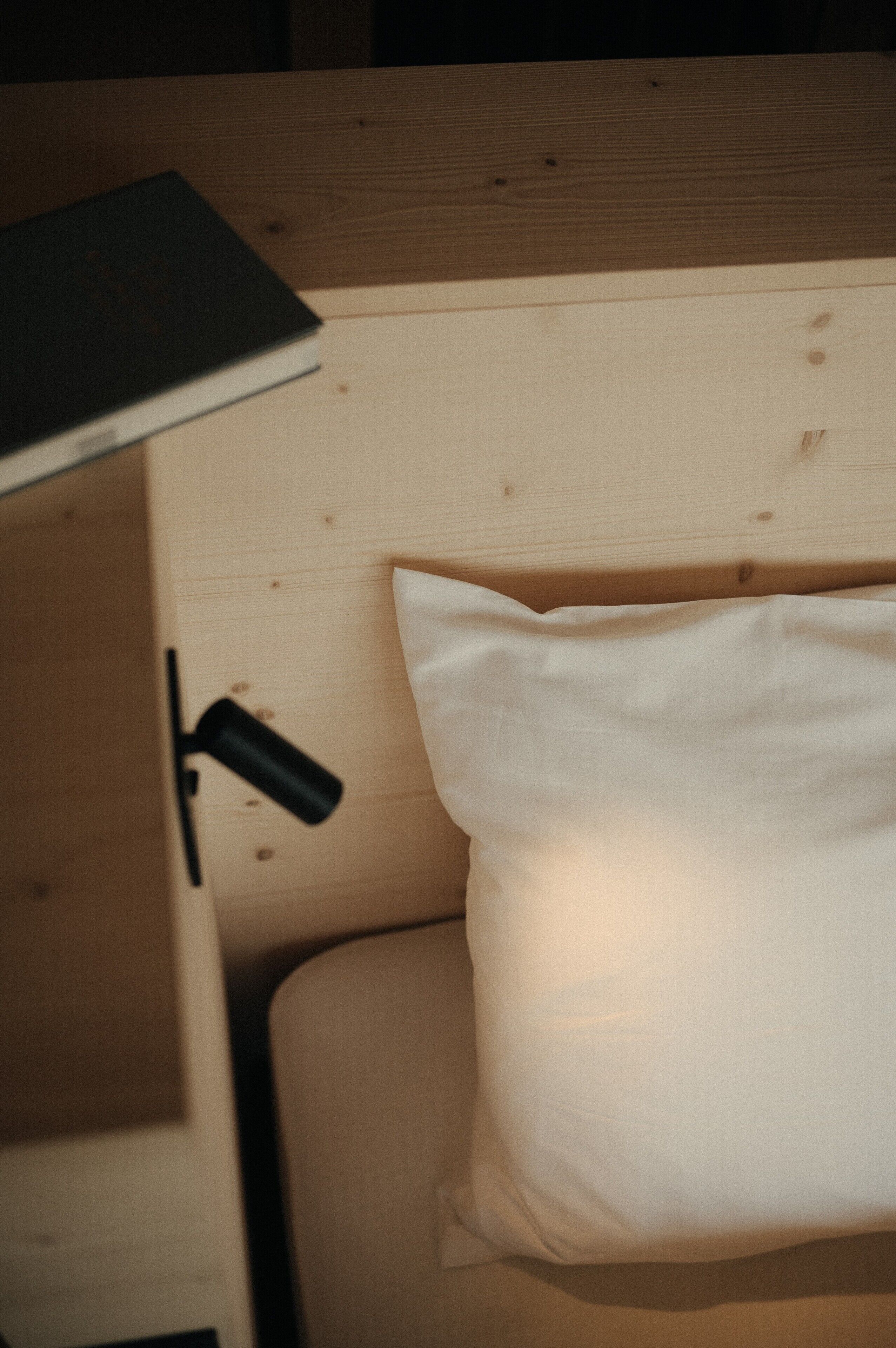 A wooden headboard with a white pillow and a black object, possibly a remote control, on a wooden surface.
