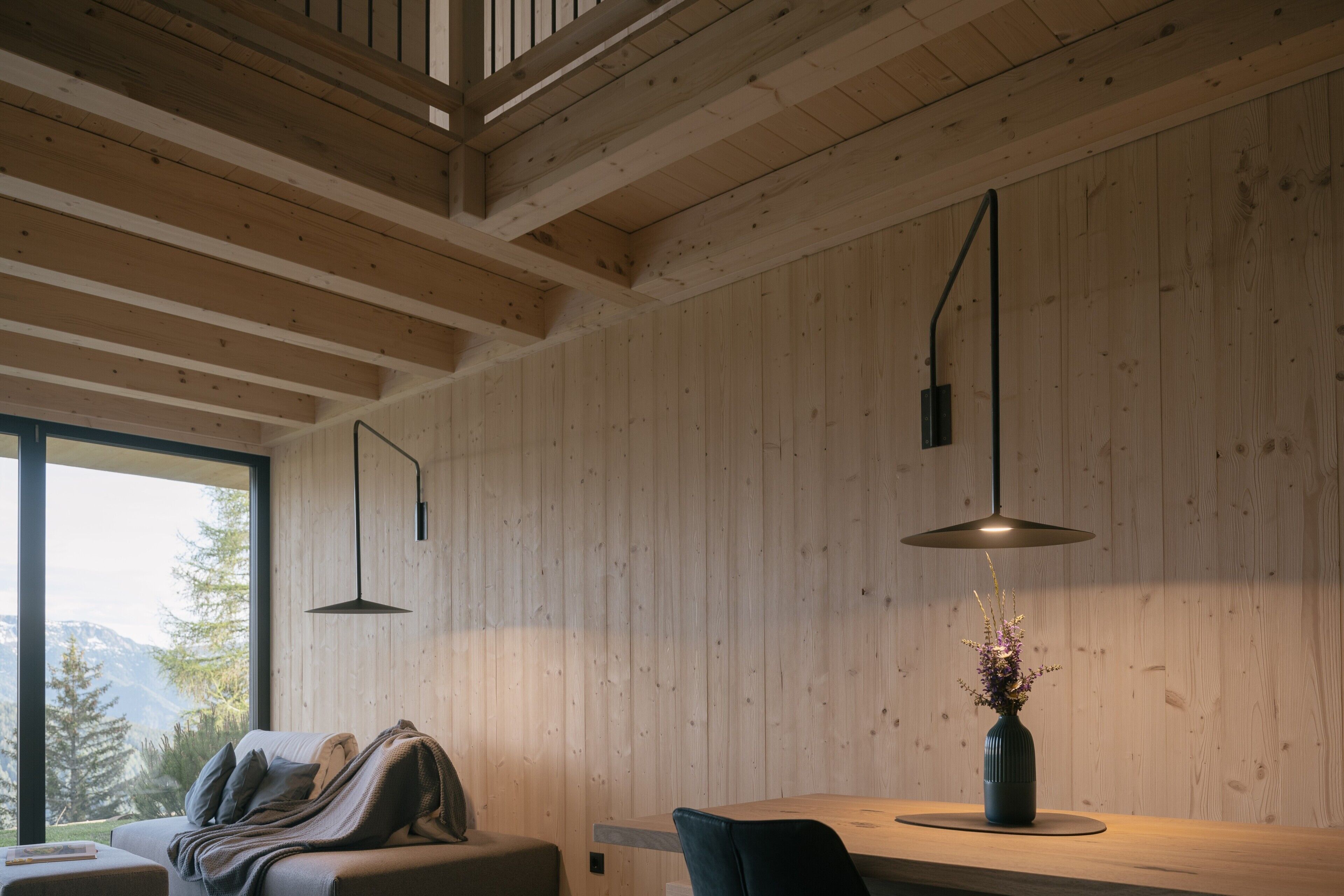 A room with wooden walls, a sofa, a table, and a vase with flowers.