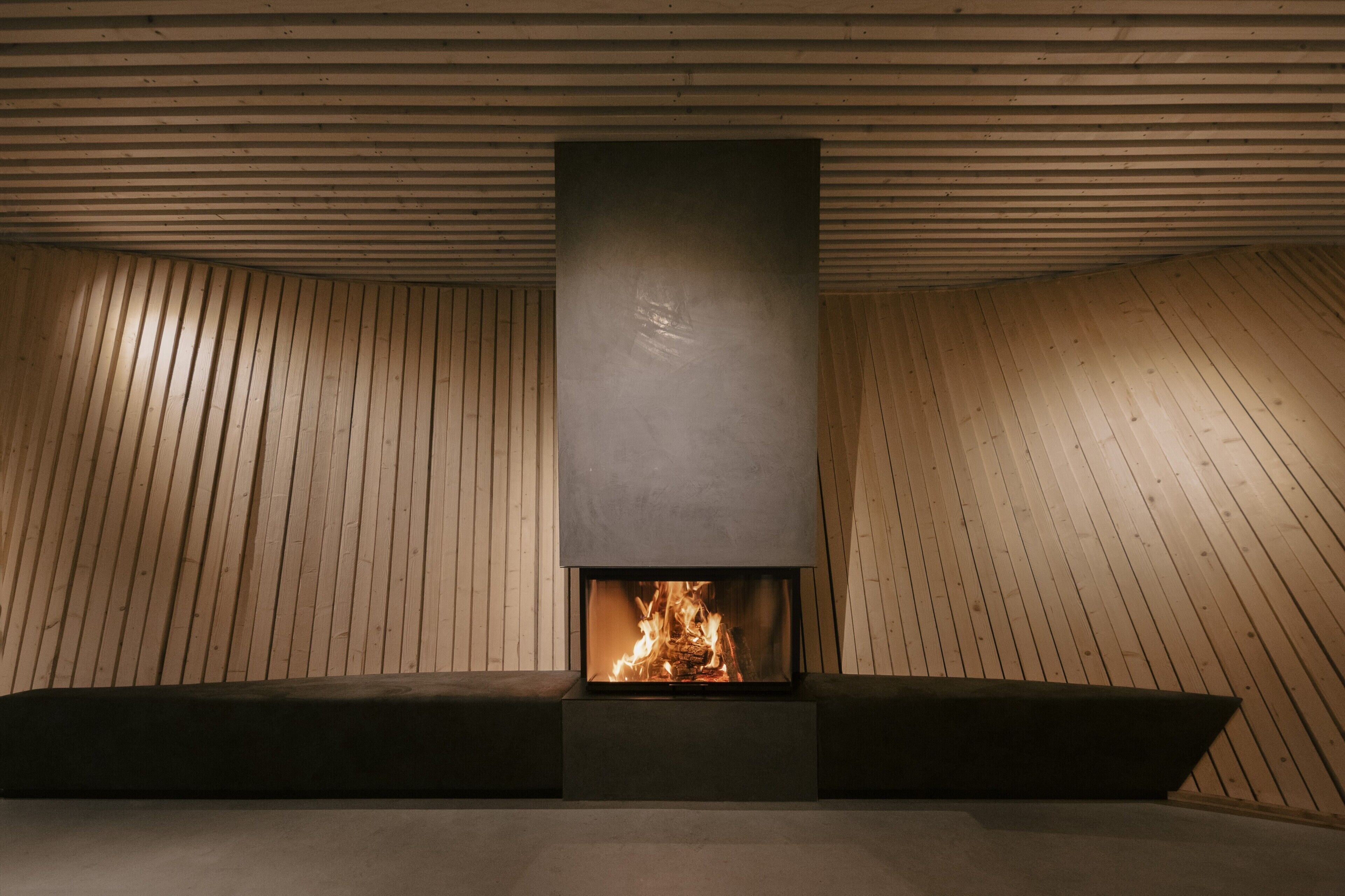 A modern fireplace with a wooden sloped ceiling and a dark, rectangular fireplace surround.