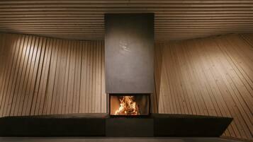 A modern fireplace with a wooden sloped ceiling and a dark, rectangular fireplace surround.