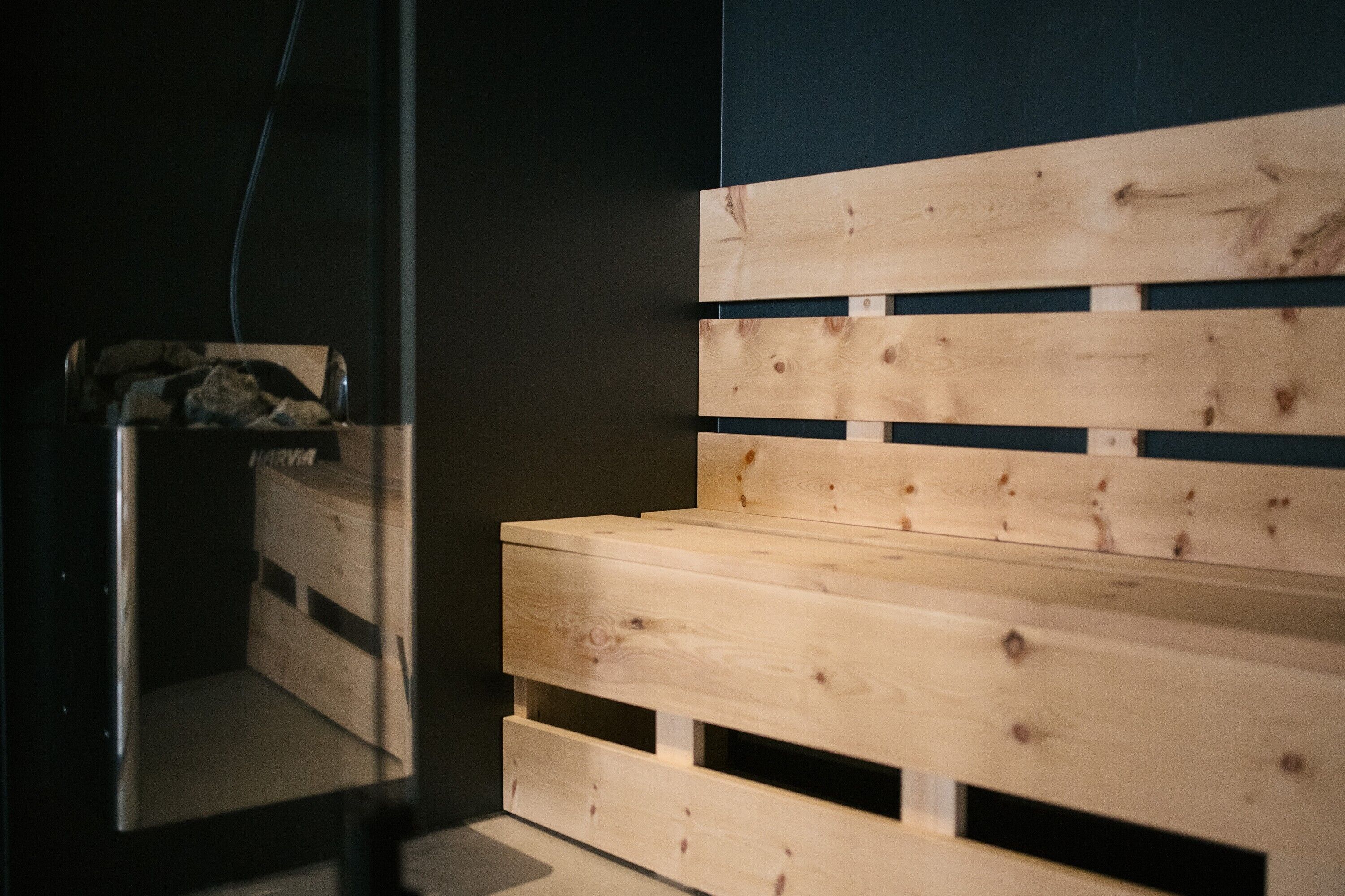 A wooden bench with horizontal slats and a dark wall in the background.