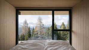 A bedroom with a large window, wooden walls, and a bed.