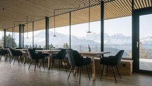 Un comedor moderno con mesas y sillas, ventanas amplias con vistas a la montaña y un techo de madera.