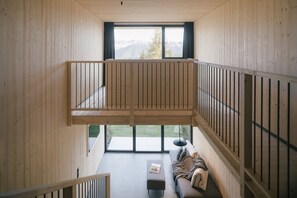 A wooden interior with a balcony, a sofa, and a window overlooking a mountain.