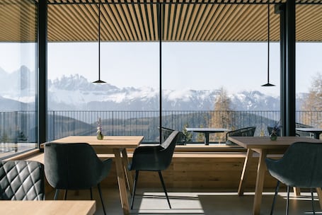 A modern dining area with wooden tables and chairs, large windows with a mountain view, and pendant lighting.