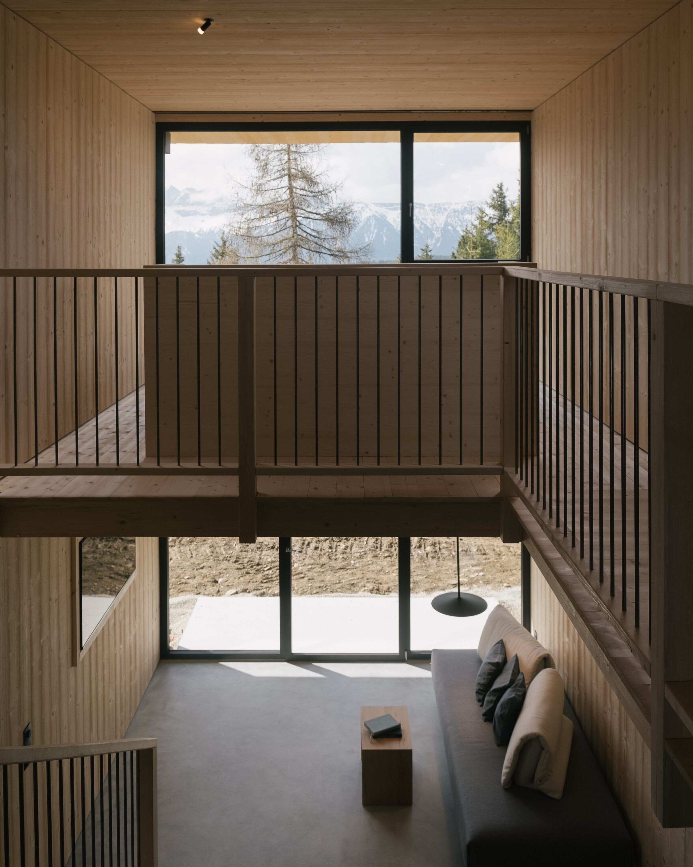 Een modern interieur met een houten vloer, een bank met kussens, een kleine tafel en uitzicht op bergen door grote ramen.