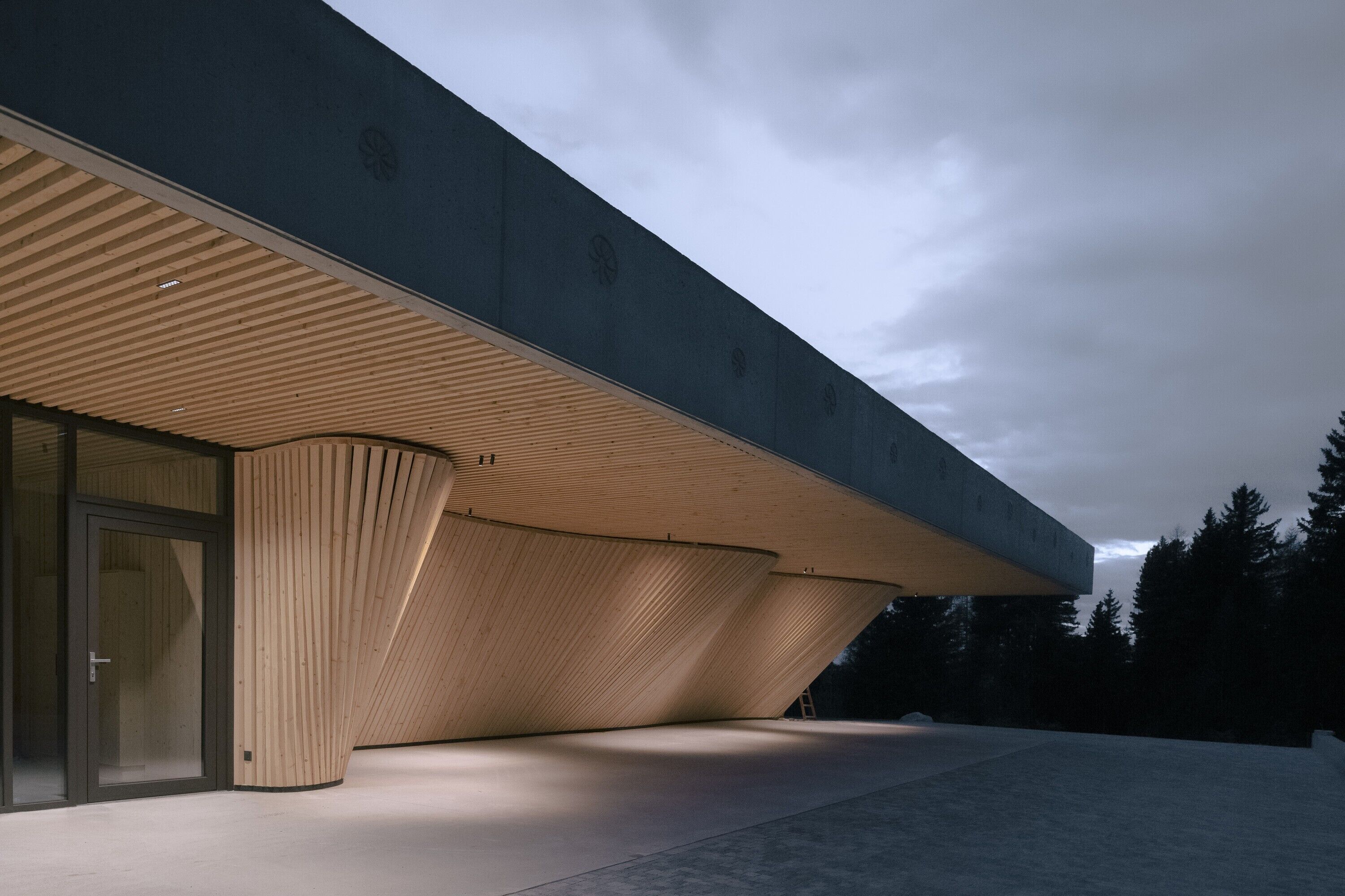 Un bâtiment moderne doté d’un toit en pente, de grandes fenêtres en verre et d’une façade en béton.