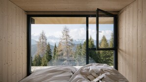 A bedroom with a large window, wooden walls, and a bed with a book.