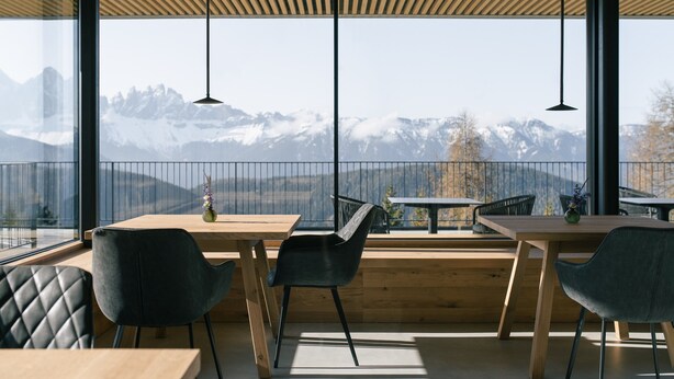 A modern dining area with wooden tables and chairs, large windows with a mountain view, and pendant lighting.