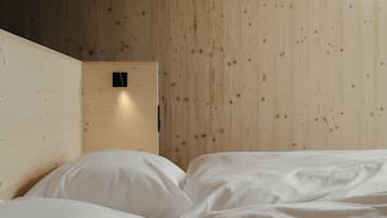 A room with a wooden wall, a bed with white bedding, and a small black object on the wall.