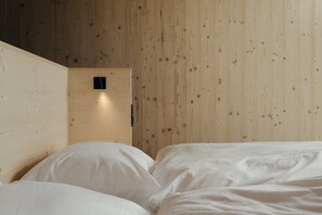 Ein Zimmer mit einer Holzwand, einem Bett mit weißer Bettwäsche und einem kleinen schwarzen Gegenstand an der Wand.