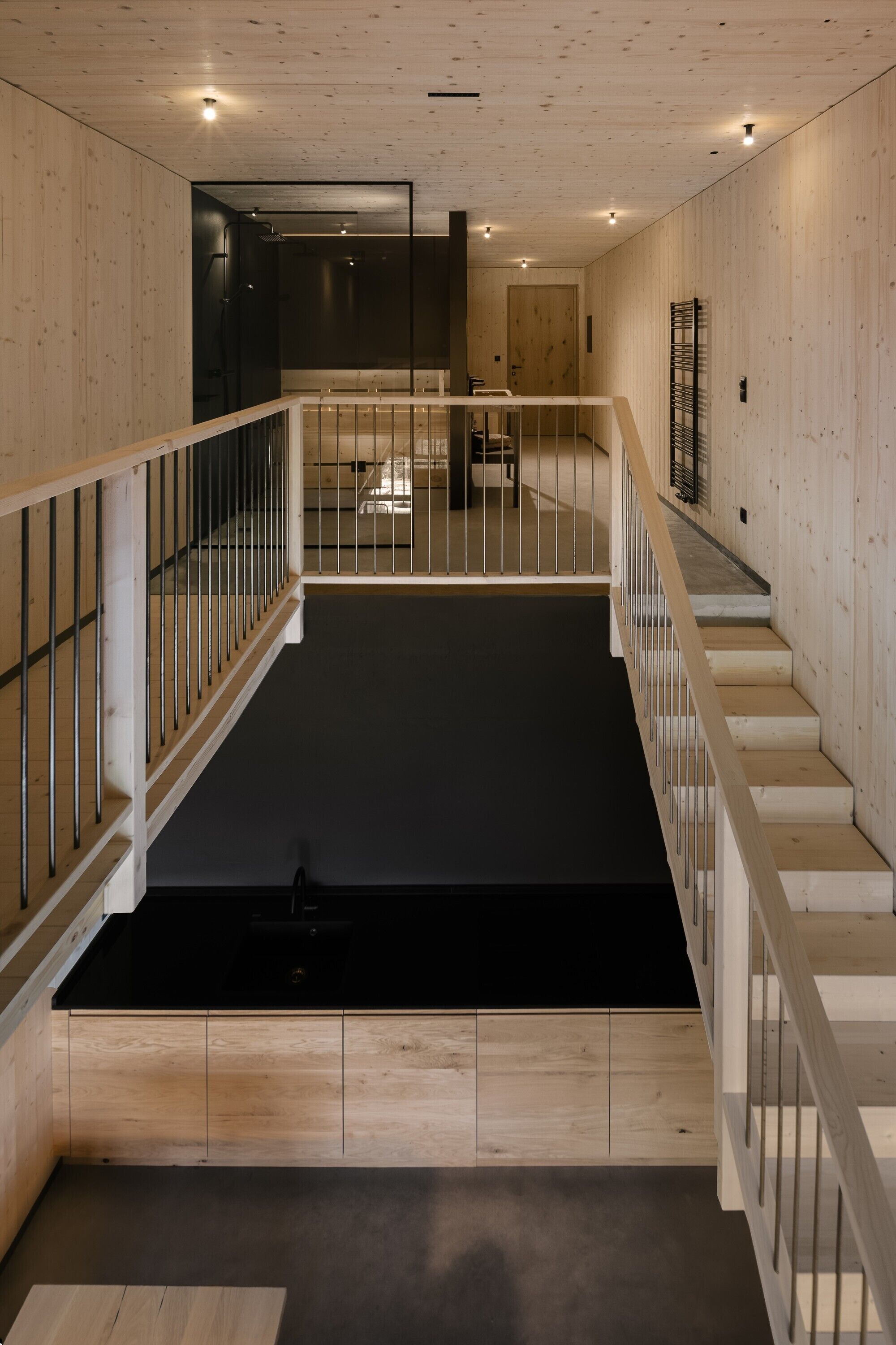 Un intérieur moderne avec un plancher en bois, un espace central de couleur noire et un escalier doté de rampes blanches.