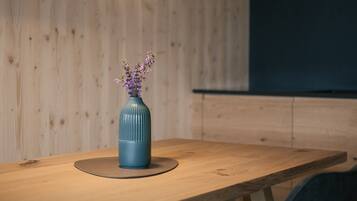 Une table de salle à manger en bois, ornée d’un vase de fleurs, un luminaire suspendu moderne et une chaise de couleur sombre.