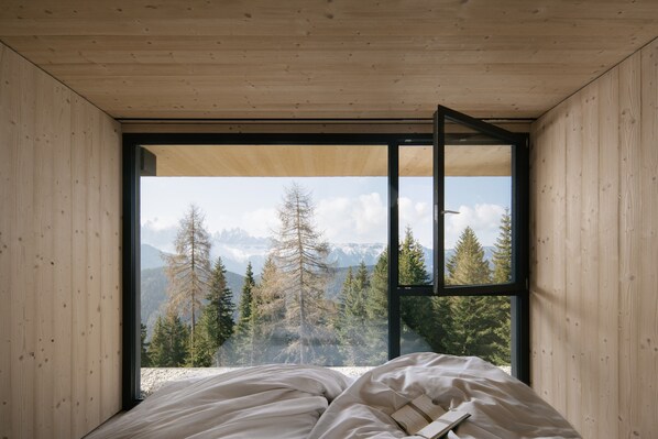 A bedroom with a large window, wooden walls, and a bed with a book.
