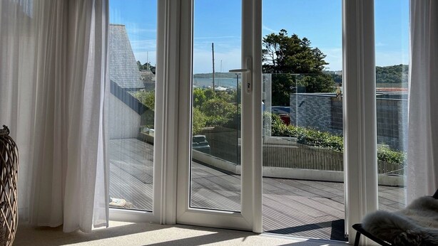 A room with large sliding glass doors leading to a balcony, a wicker chair, and a view of a residential area.
